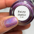 Nail polish with glittery pink and purple design held by a hand, next to a jar labeled 'Fairy Static'.