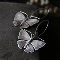 Flat view of Sterling silver moth earrings with detailed wings hanging from silver French hook ear wires.
