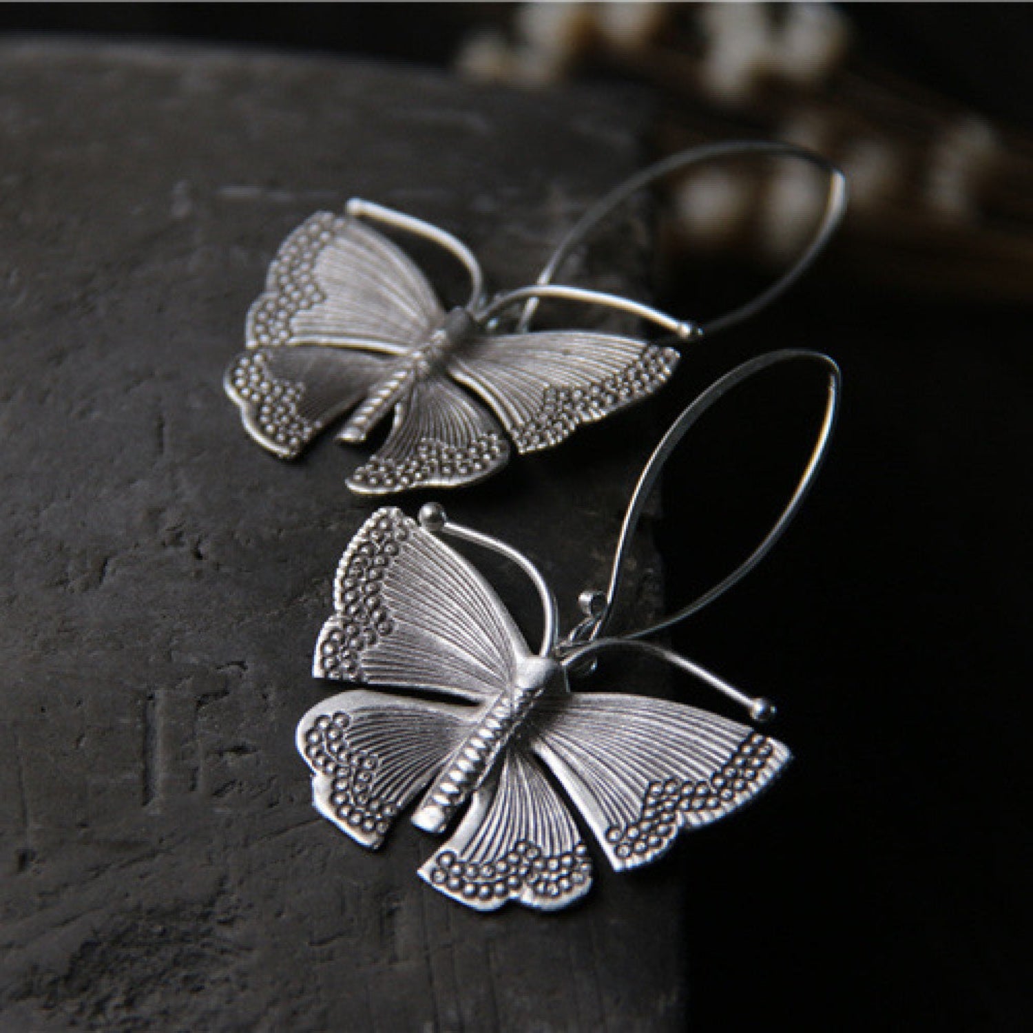 Flat view of Sterling silver moth earrings with detailed wings hanging from silver French hook ear wires.