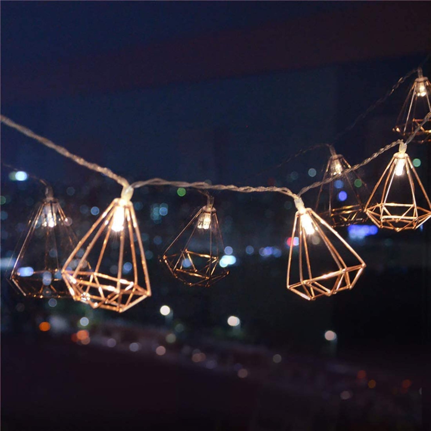 String of geometric lantern lights against a night sky with blurred lights in the background.