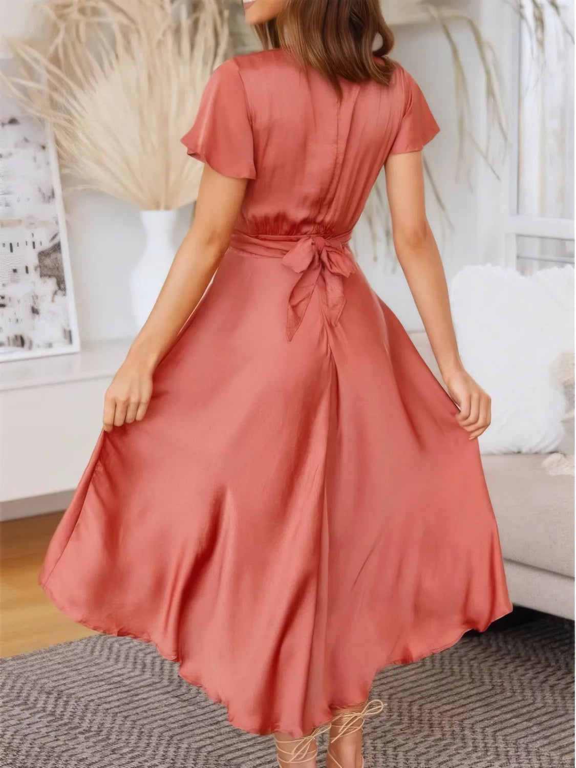 Back view of the coral high‑low dress on the model, showing the crisscross tie‑back and high‑low hemline.