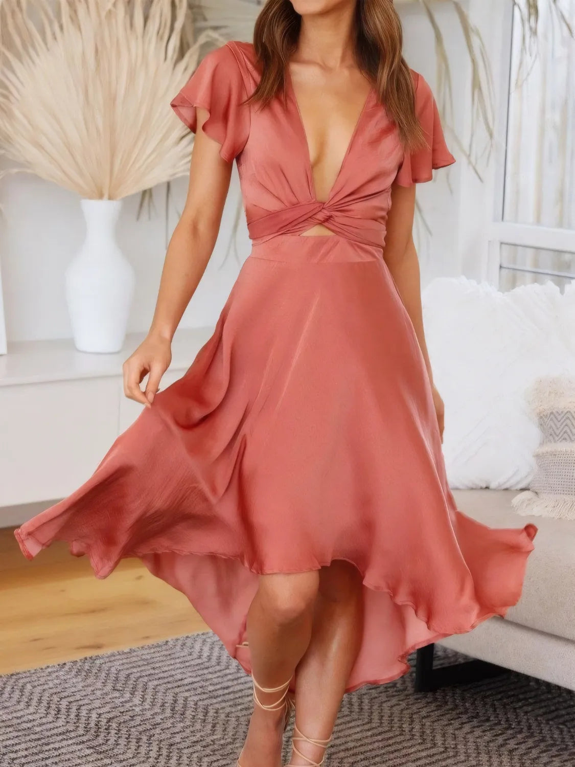 Model wearing the coral high‑low plunge dress from the front, showing the flutter sleeves and flowing hem.