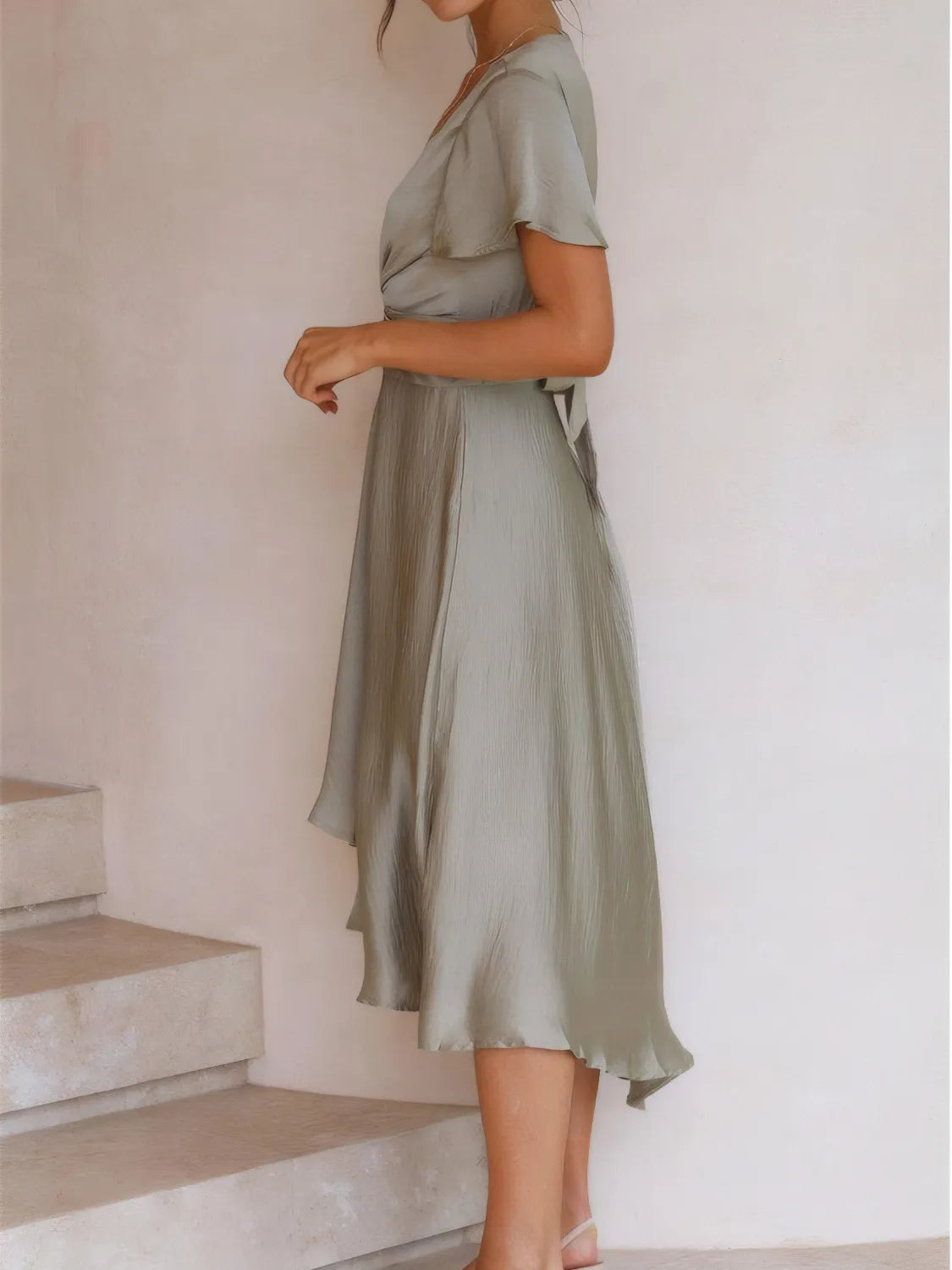 Side view of the sage high‑low dress on the model, highlighting the flowing silhouette and high‑low hem.