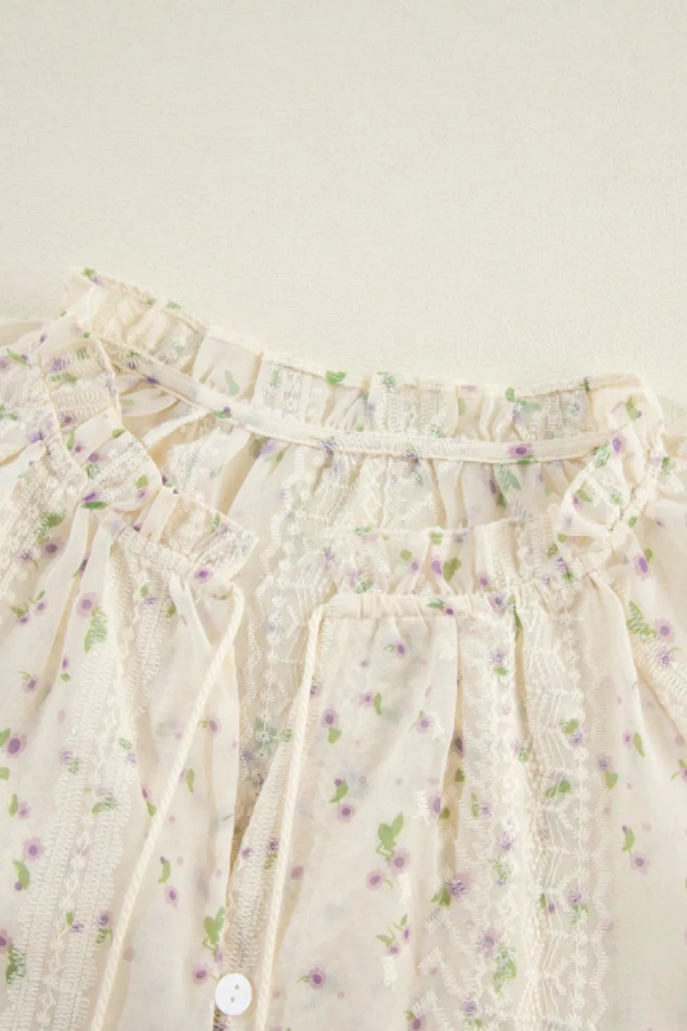 Close‑up of the tie‑neck bow and lace frill neckline on the printed blouse.