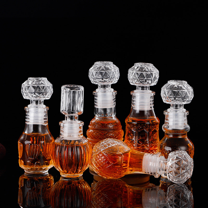 Set of five mini glass decanter‑style bottles in assorted patterns — Mossroot Grove (earth), Winterwhisper Crystal (snowflake), Moonspire Column (vertical), Golden Thistle Charm (pineapple), and Starshard Prism (diamond) — displayed together as whimsical apothecary wishing bottles