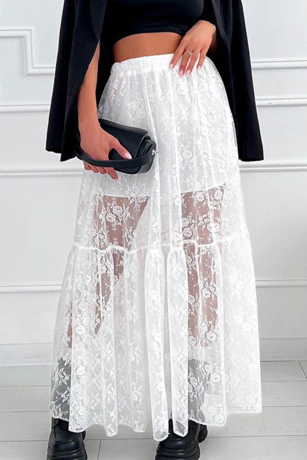 Person wearing a white lace skirt with a black top and shoes on a light background