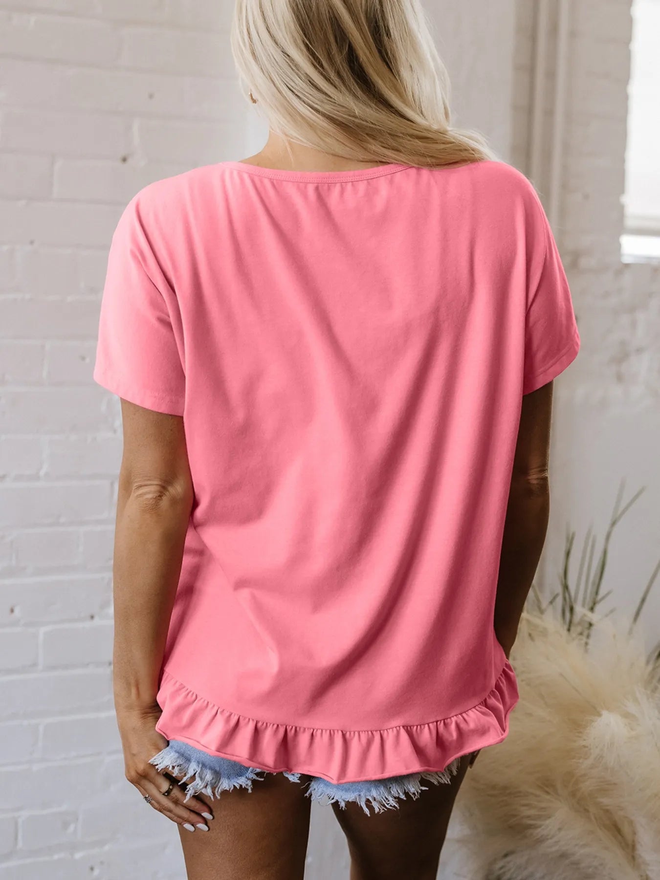 Back view of the pale blush round‑neck relaxed T‑shirt, showing the smooth fit and ruffle hem.