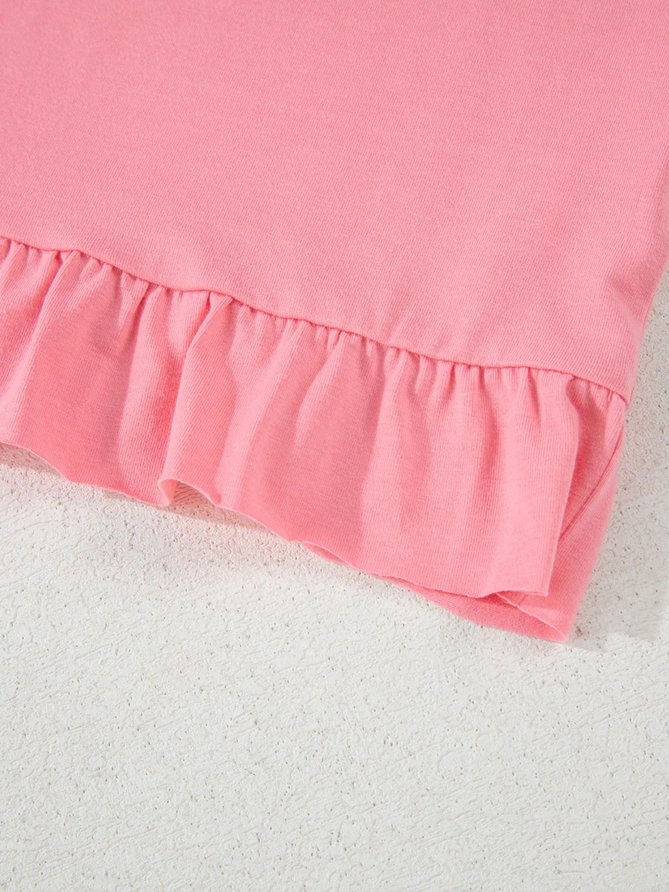 Close‑up of the ruffle hem detail on the pale blush relaxed T‑shirt.